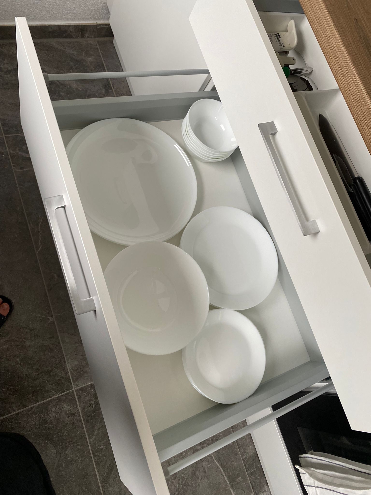A kitchen drawer with white plates and bowls.