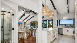 A modern kitchen with white cabinets, a marble island, and a large window.