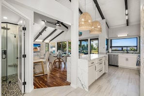 A modern kitchen with white cabinets, a marble island, and a large window.