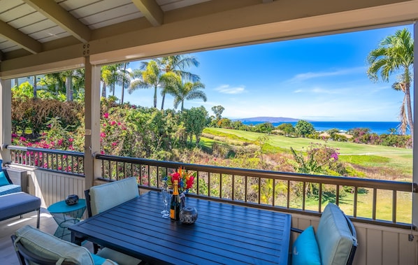 Um espaço ao ar livre coberto com mesa, cadeiras e vista para um campo de golfe e o oceano.