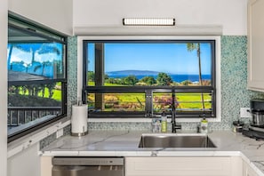 A kitchen with a large window, a stainless steel sink, a dish soap dispenser, and a coffee maker.