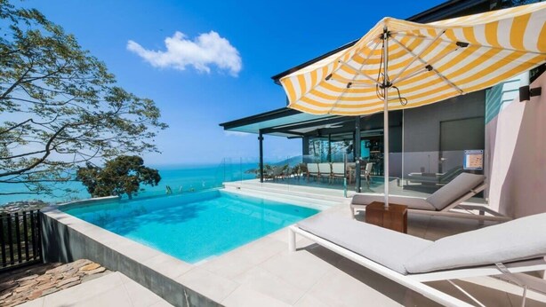 A poolside area with a view of the ocean, a lounge chair, and a striped umbrella.