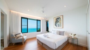 A bedroom with a large bed, a chair, a small table with a vase, and a painting on the wall.