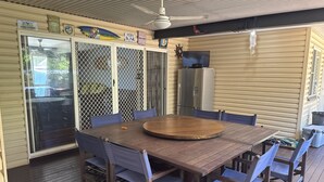A covered patio with a wooden table and chairs, a ceiling fan, and a TV mounted on the wall. - Island Home is Located on beautiful Moreton Island in the township of Kooringal (Kooringal)