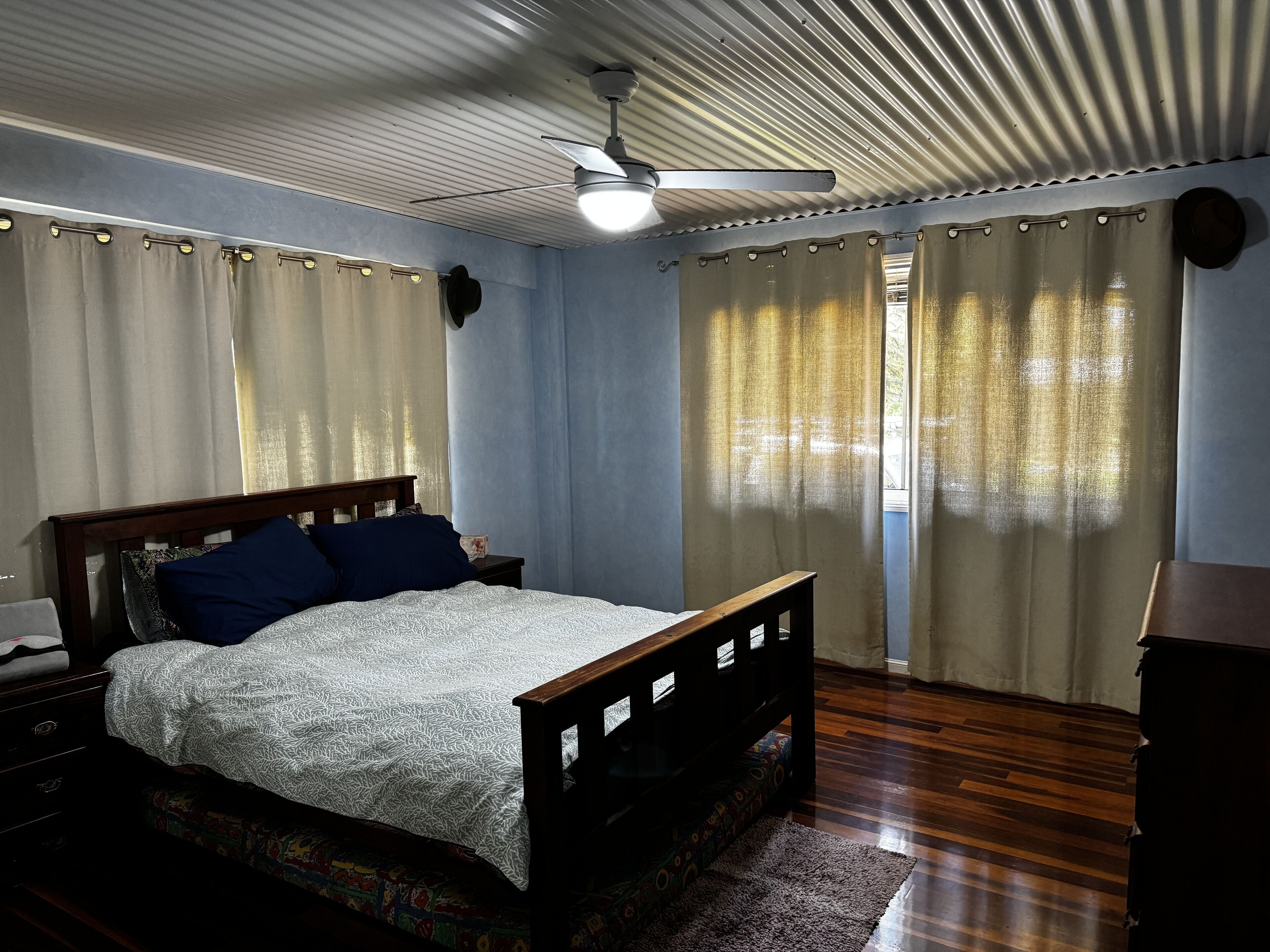 A bedroom with a wooden bed, a nightstand, a ceiling fan, and a window with curtains.