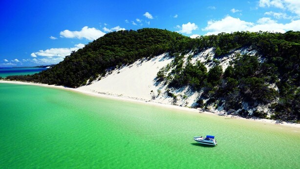 A boat on a clear turquoise sea with a white sandy beach and a forested hill in the background. - Island Home is Located on beautiful Moreton Island in the township of Kooringal (Kooringal)