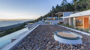 A modern house with a pool, surrounded by rocks and palm trees, overlooking a body of water. - Lime10 (Koh Samui)