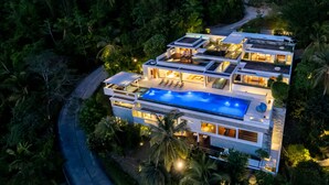 A modern multi-story house with a large swimming pool, multiple balconies, and lush surrounding vegetation. - Lime10 (Koh Samui)