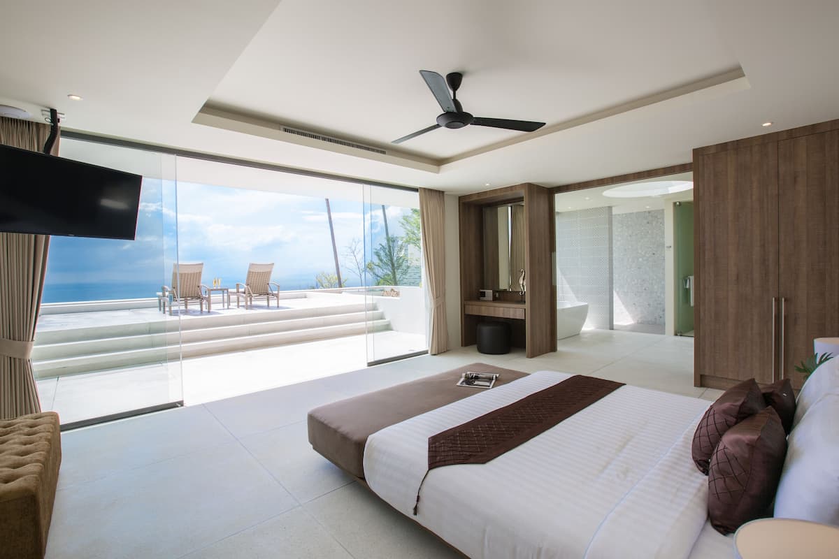 Ein modernes Schlafzimmer mit einem großen Bett, einem Deckenventilator und Meerblick.