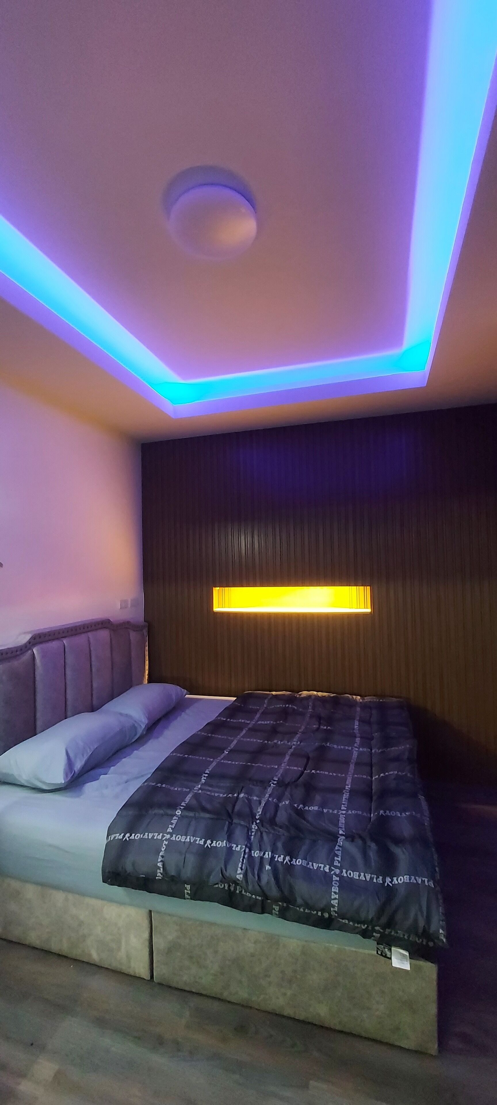 Un dormitorio moderno con una cama, una lámpara de techo y una luz fijada a la pared.
