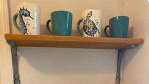 Et tekøkken med kaffemaskine, skraldespand og en hylde med dekorative krus.