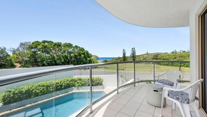 Un balcon doté d’une balustrade en verre, une piscine et deux chaises blanches avec des coussins à motifs.
