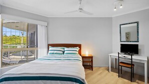 Une chambre à coucher comprenant un lit, un bureau, une chaise, un téléviseur, un ventilateur de plafond et une fenêtre donnant sur un paysage verdoyant.