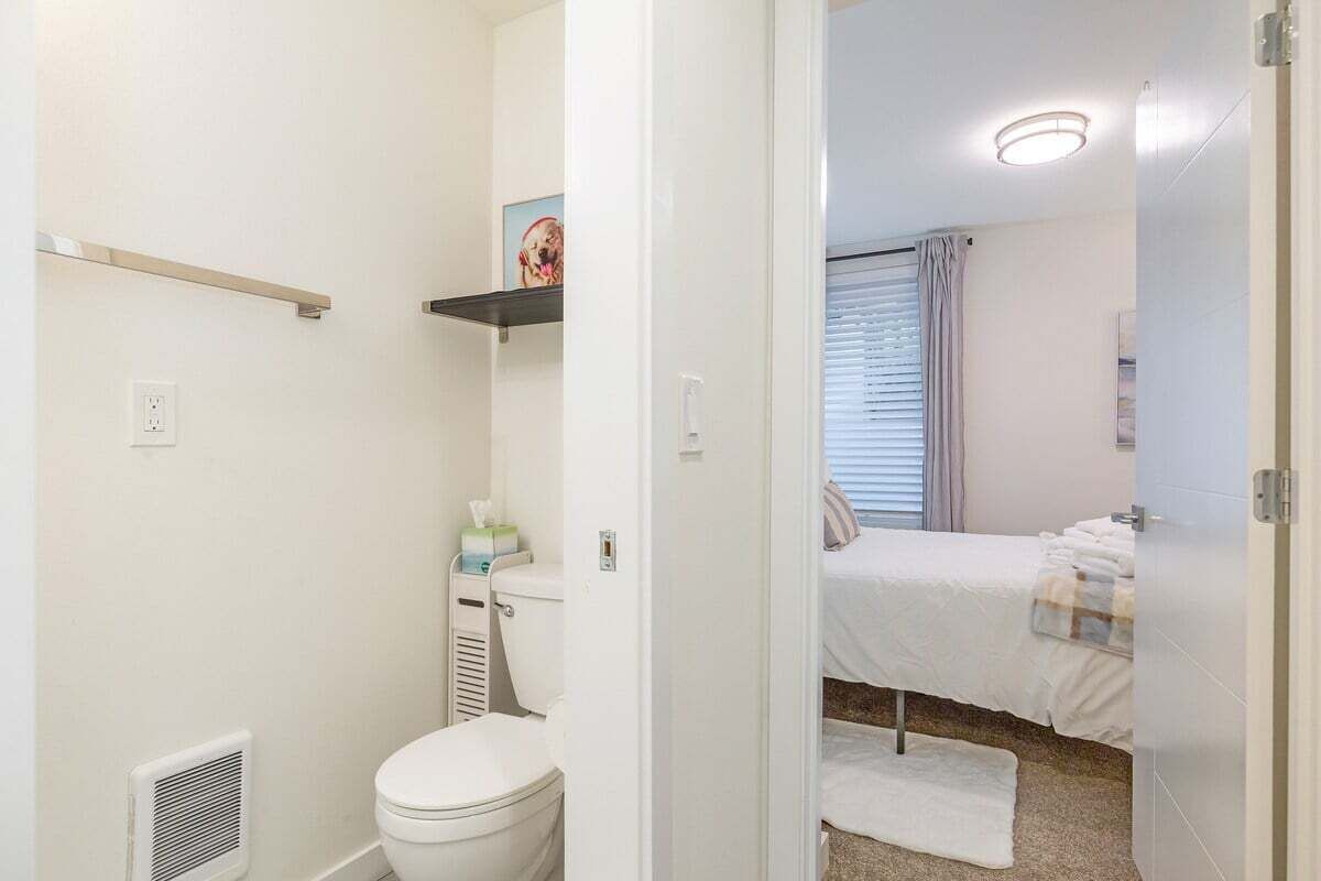 Ein kleines, sauberes Badezimmer mit Toilette, einem Ablagefach über der Toilette und einem weißen Heizkörper.