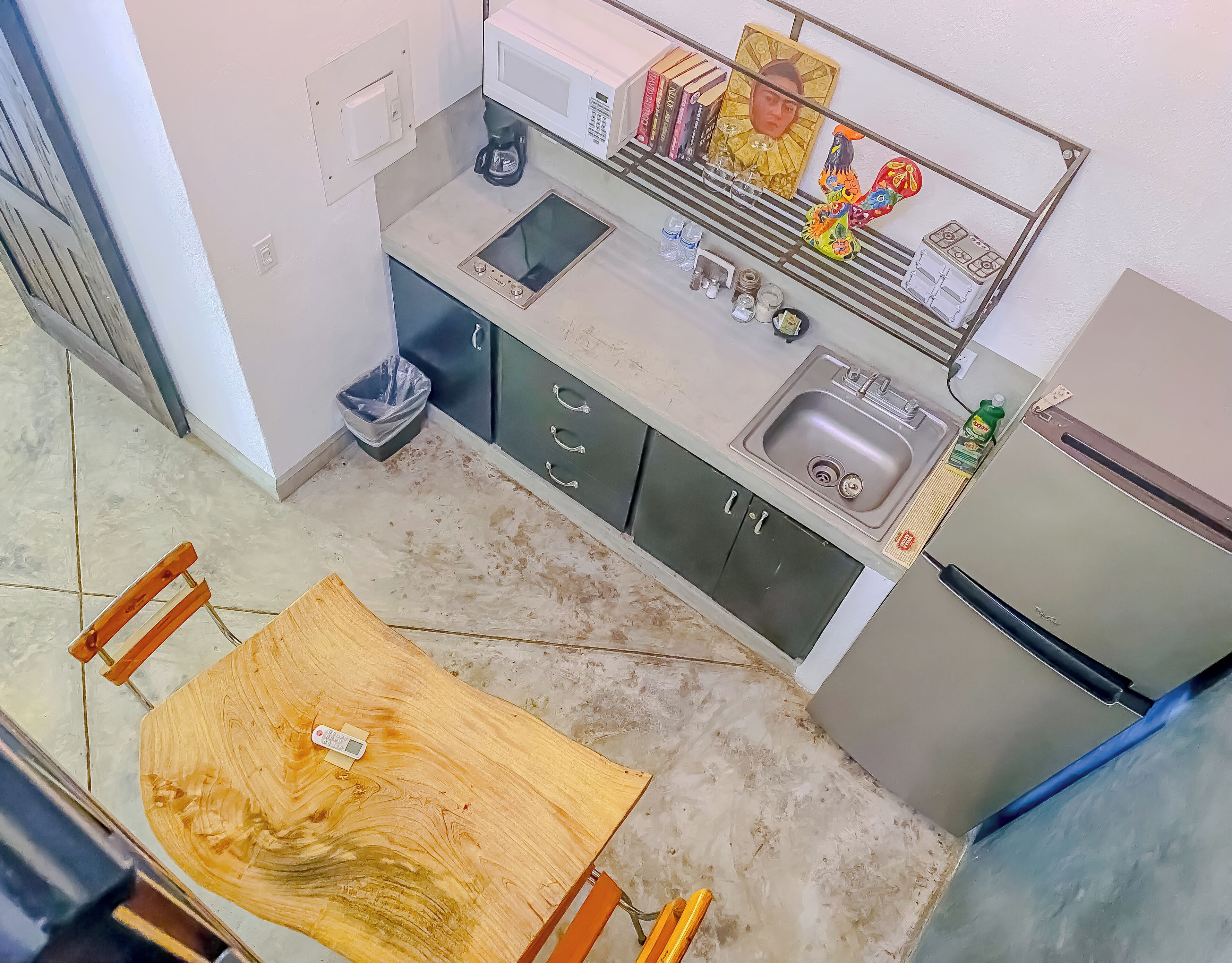 A compact kitchen with a microwave, sink, and refrigerator. There is a small dining table with a chair.