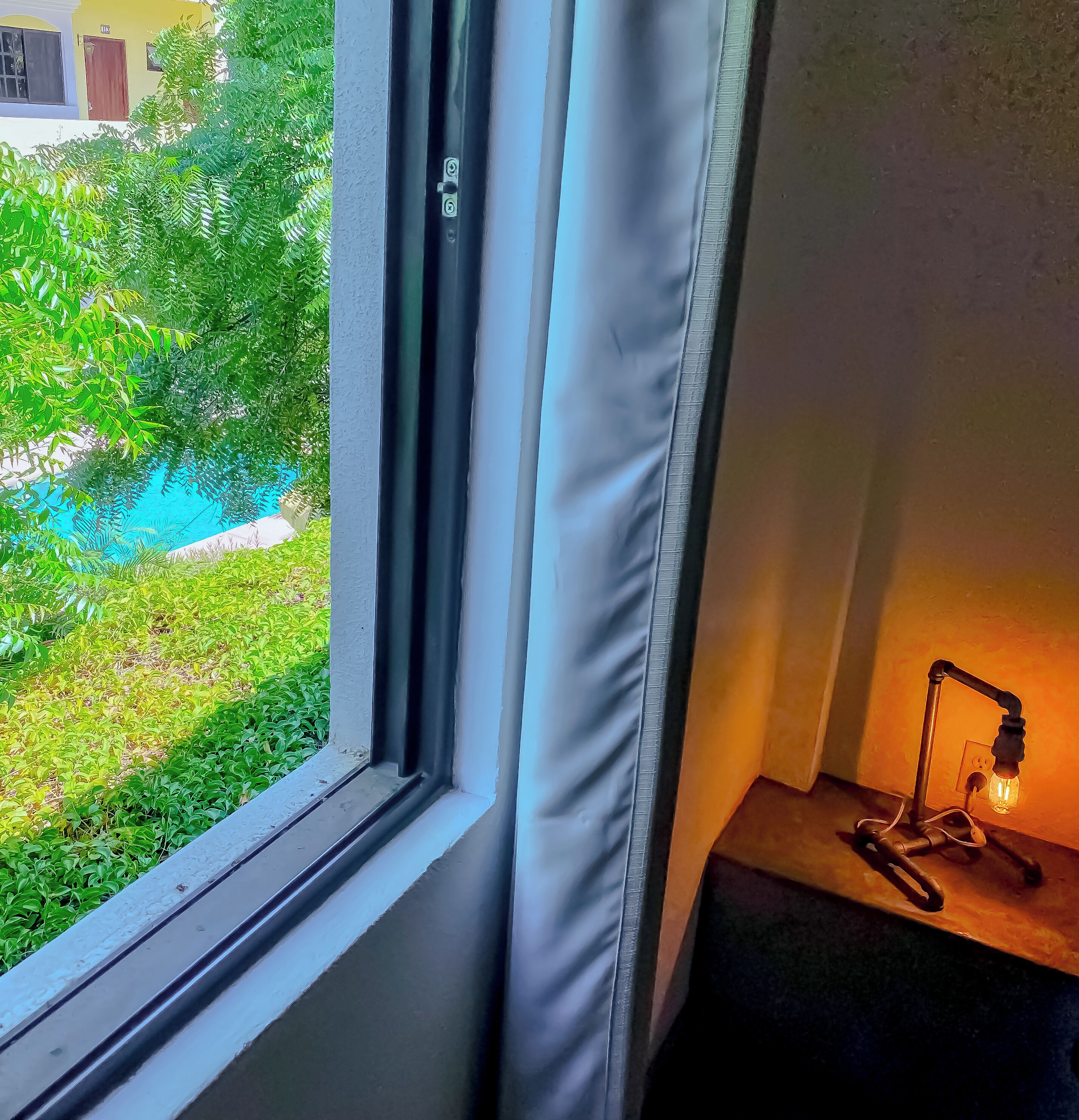 Een raam met uitzicht op een tuin en een kleine tafel met een lamp.