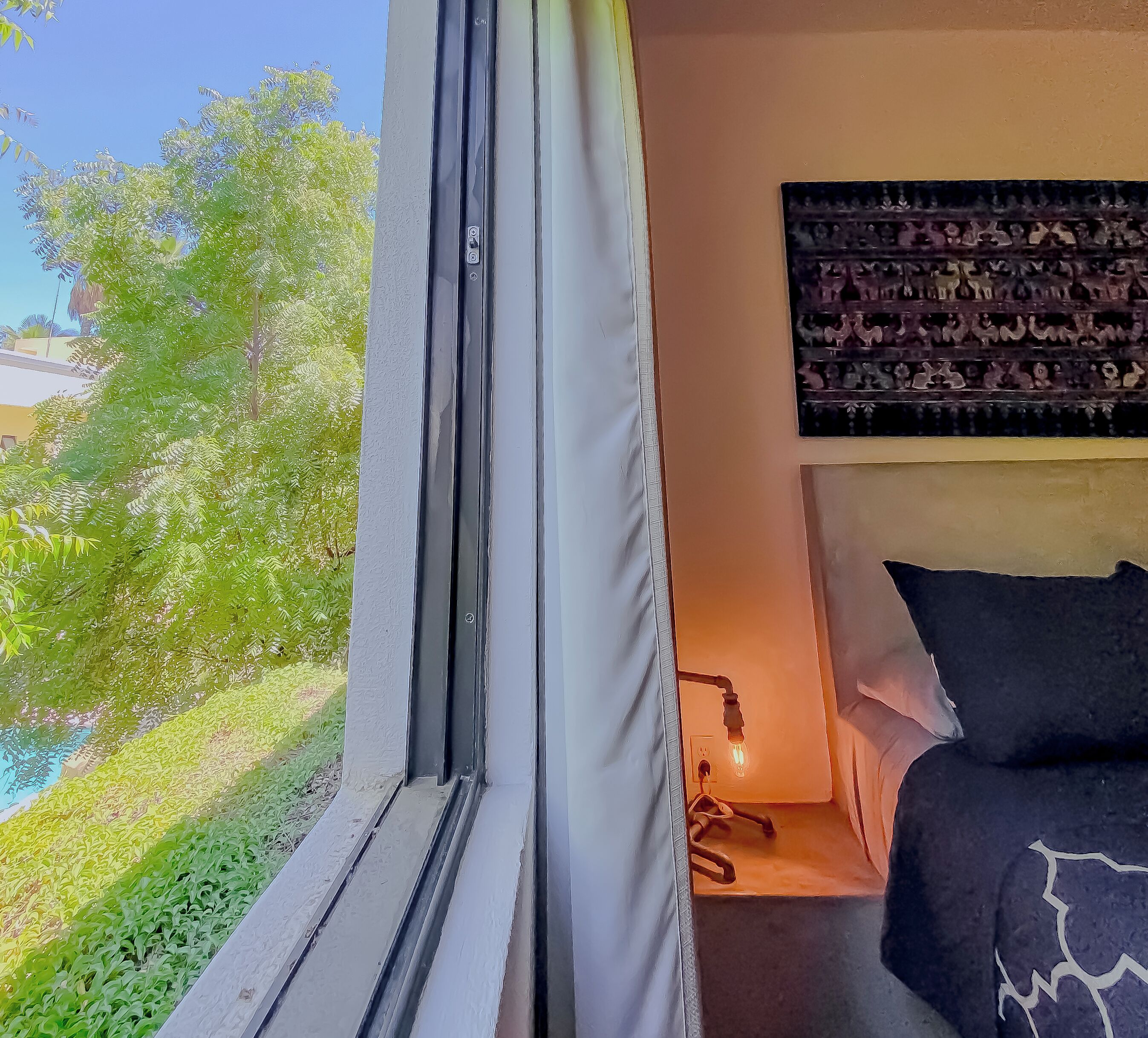 A bedroom with a bed, a bedside lamp, and a view of greenery outside.