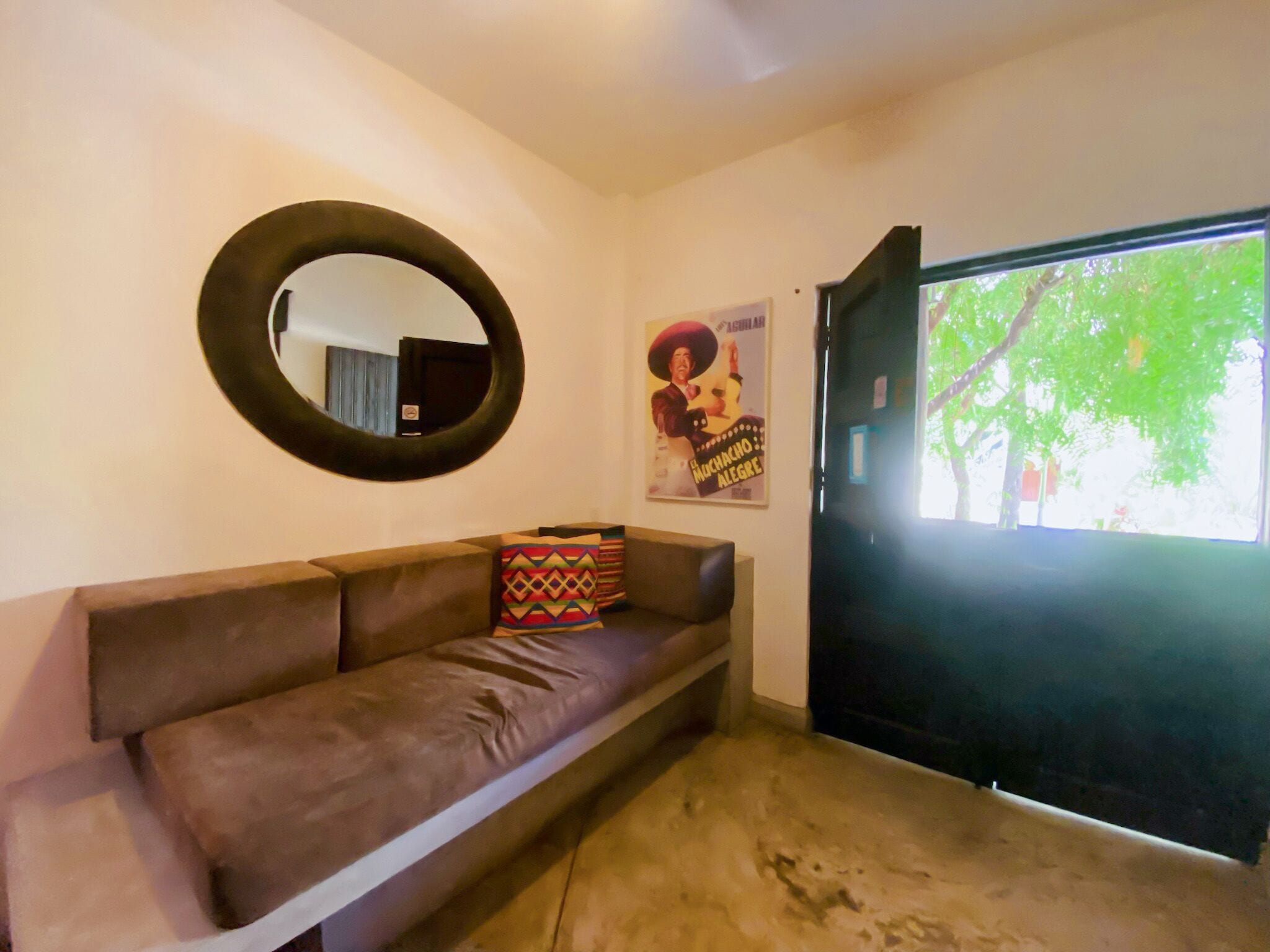 A living room with a brown sofa, a round mirror, and a poster on the wall.