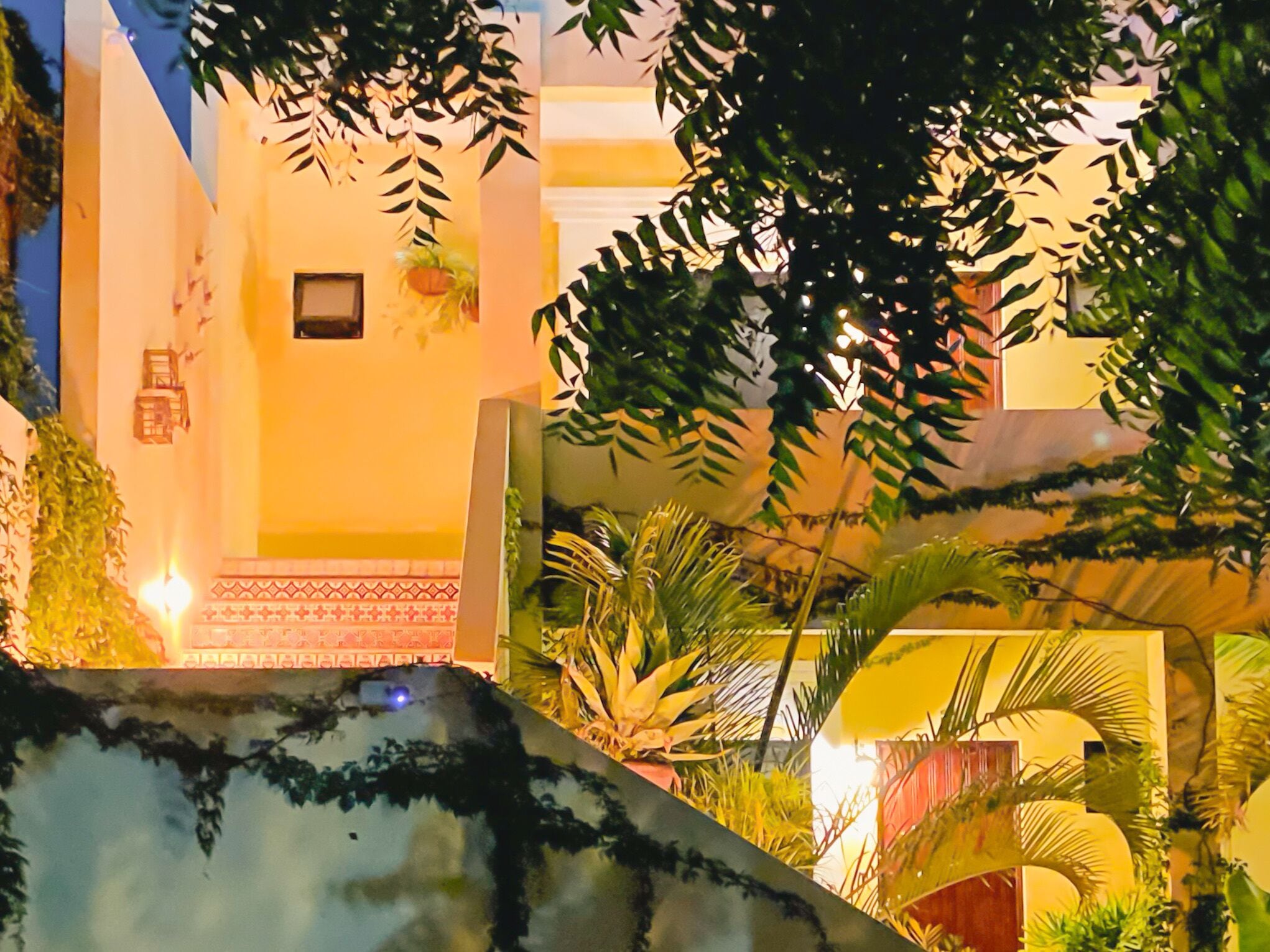 Un patio con una fuente, plantas en macetas y un edificio con piso de baldosas y una ventana pequeña.