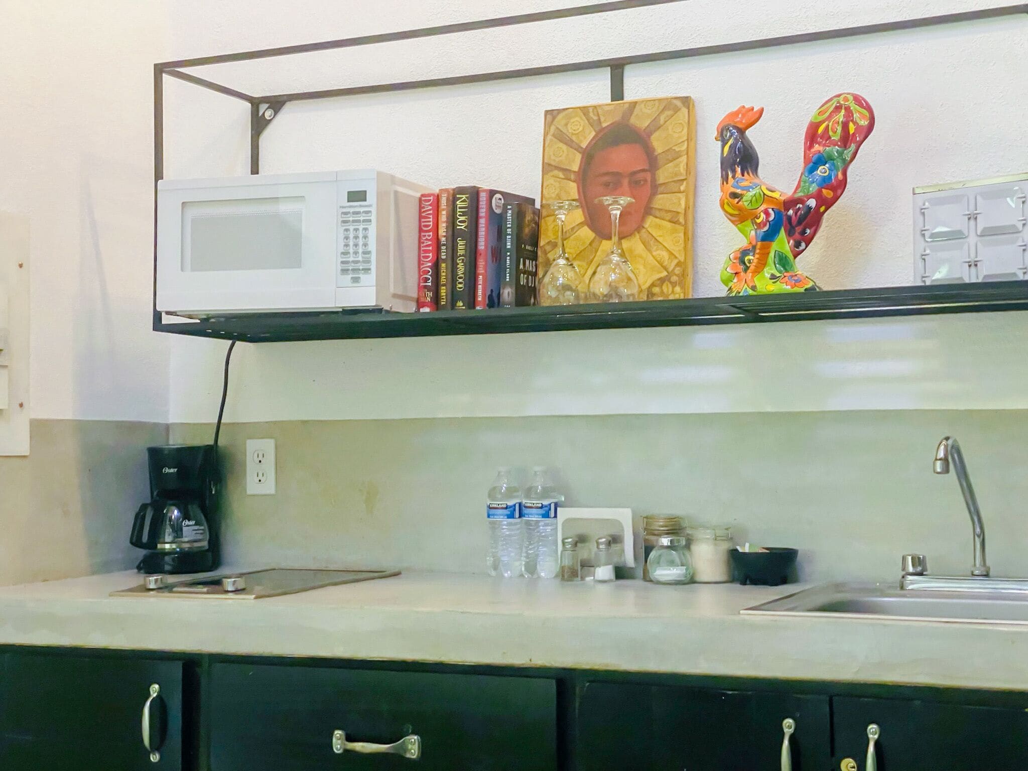Una cocina equipada con microondas, libros, cafetera y lavabo.