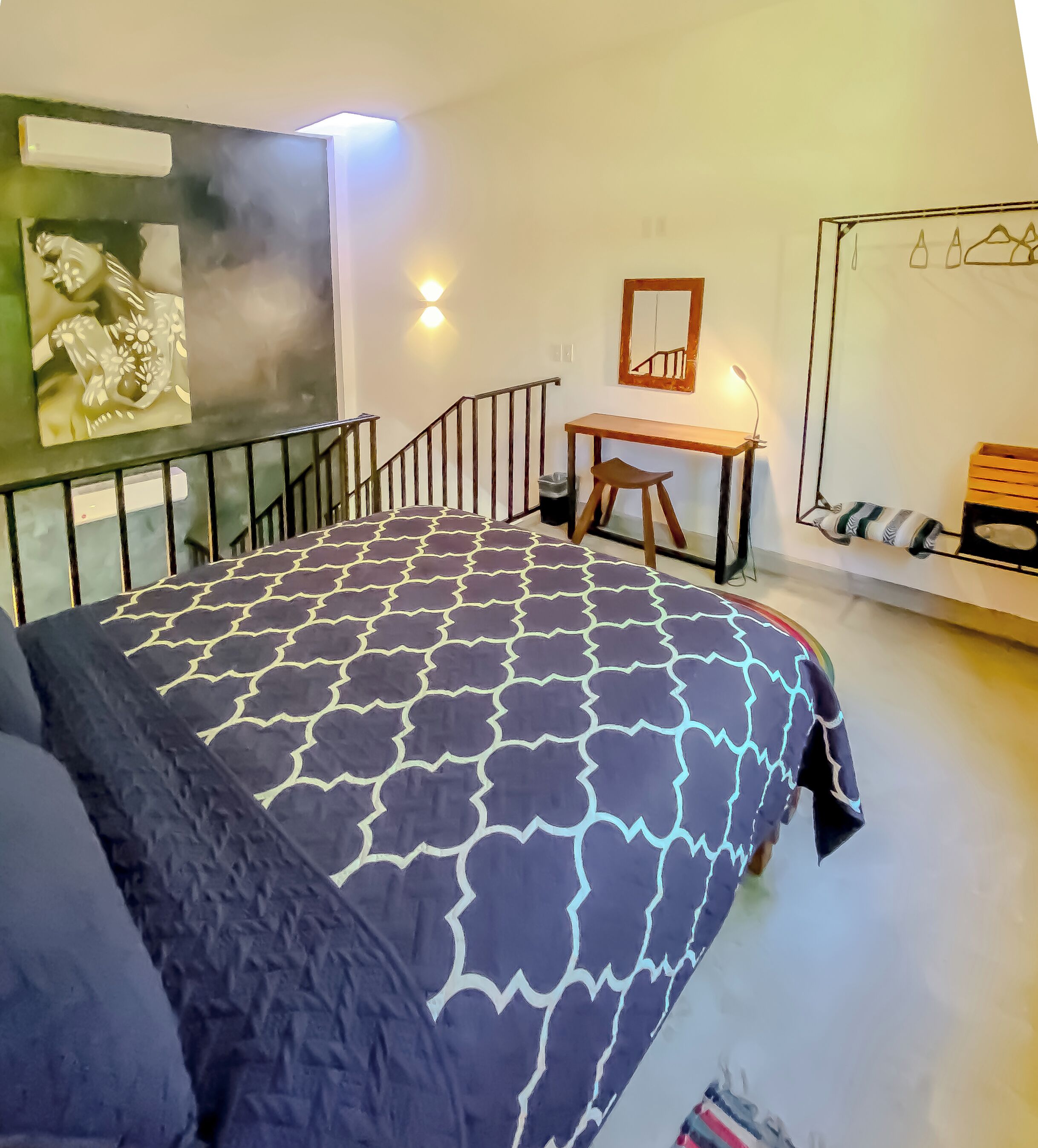 A bedroom with a patterned bedspread, a desk with a chair, a mirror, and a shoe rack.