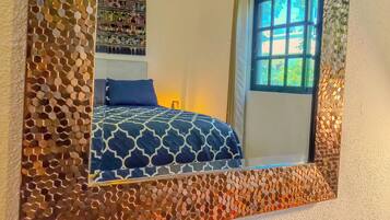 Un dormitorio con un espejo grande, una cama con colcha estampada y una ventana que da a zonas verdes.