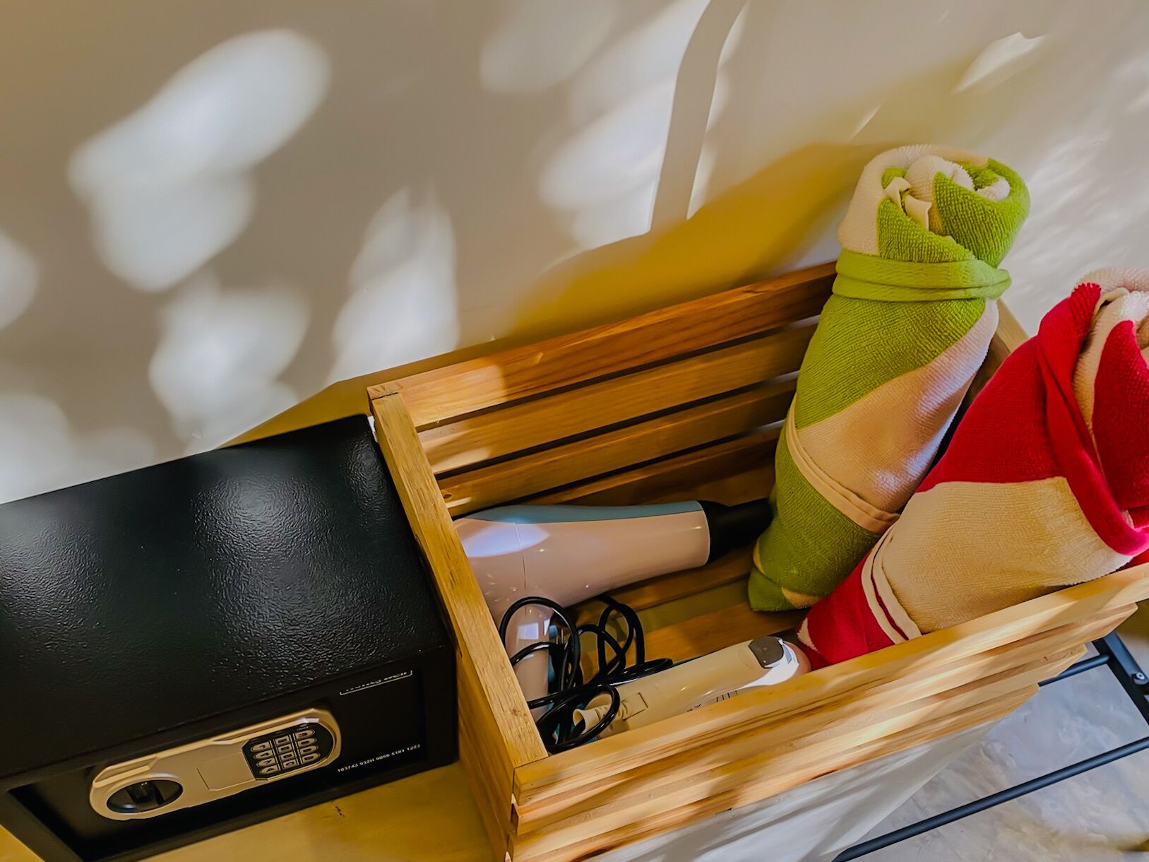 Un cofre de madera con un dispositivo electrónico negro, una toalla verde y roja, y un par de auriculares.