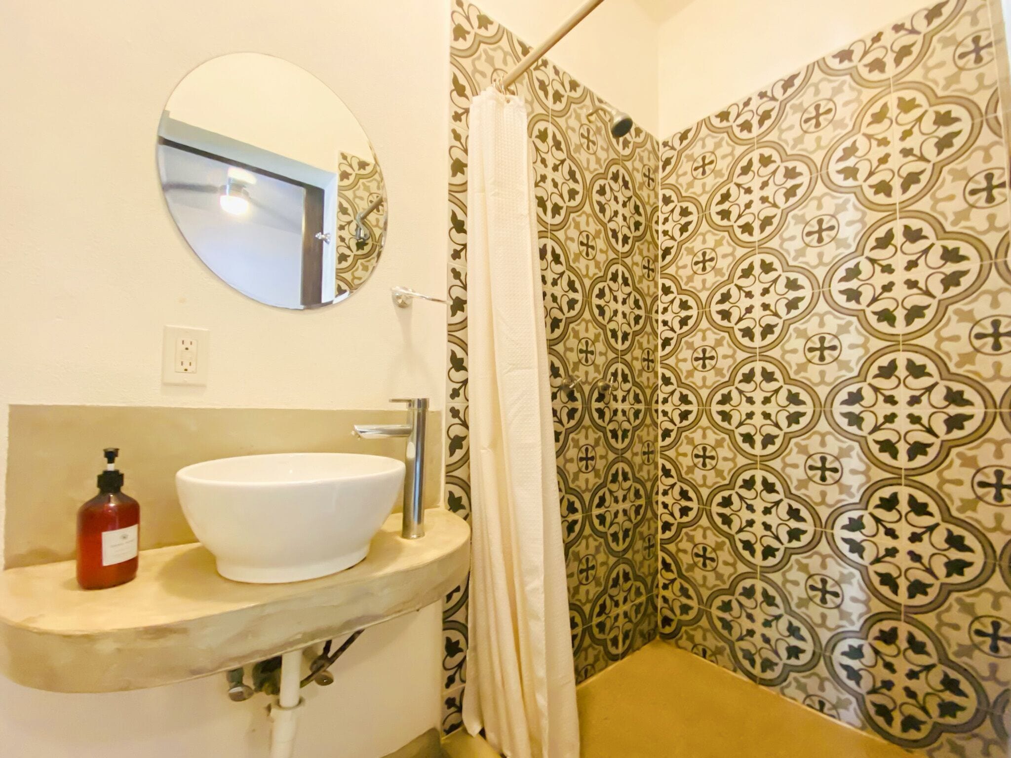 A bathroom with a round mirror, a white sink, a bottle of hand soap, and patterned tiles.