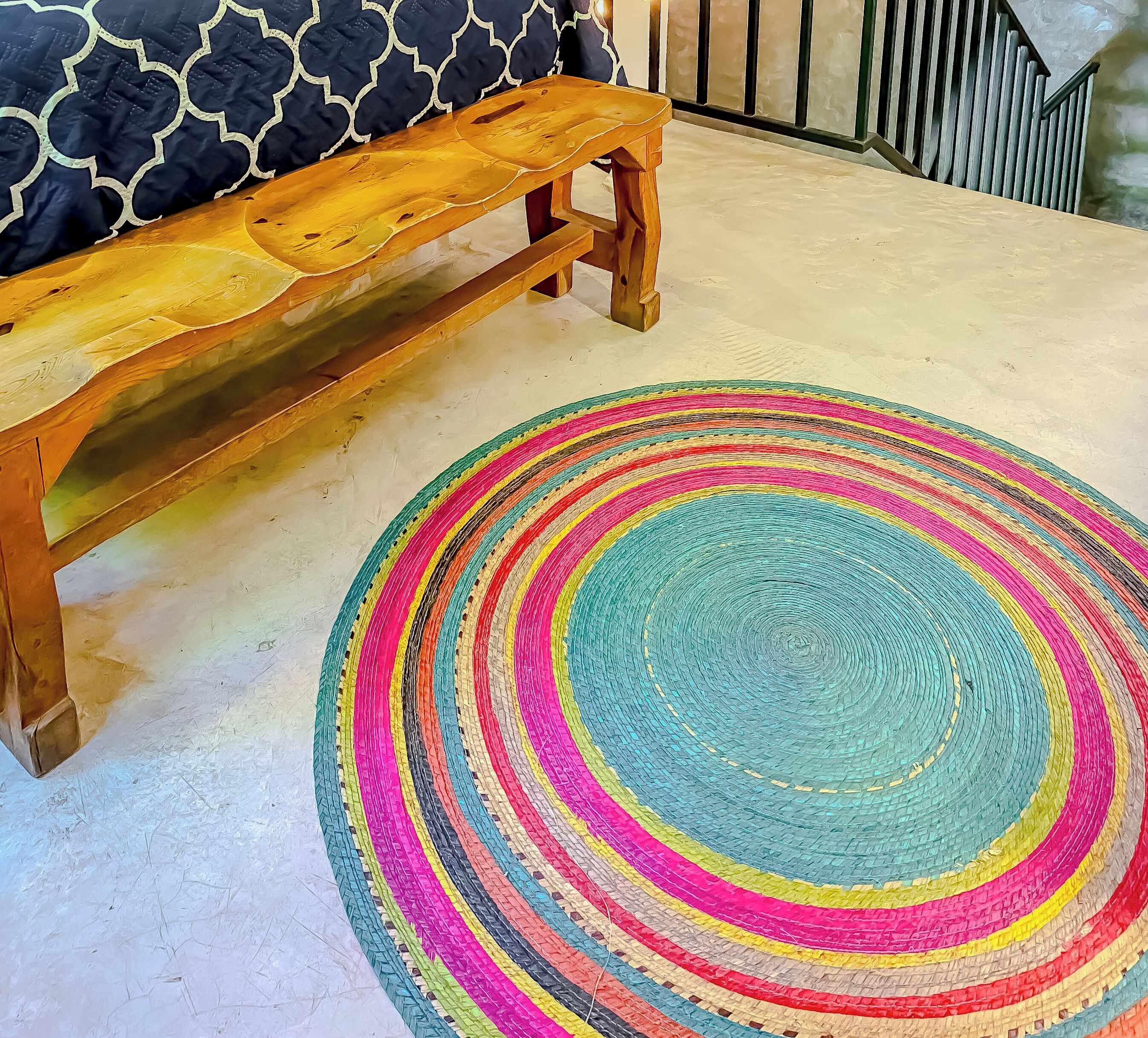A wooden bench and a colorful circular rug in a room with a patterned wall.