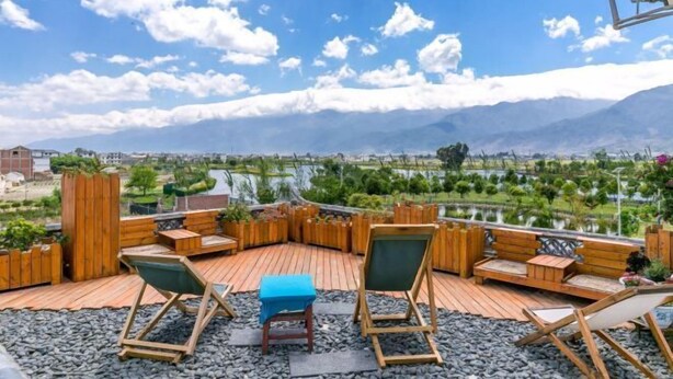 A wooden deck with seating and a table, overlooking a scenic landscape with mountains and a body of water. - Mumu Hotel (Dali City)