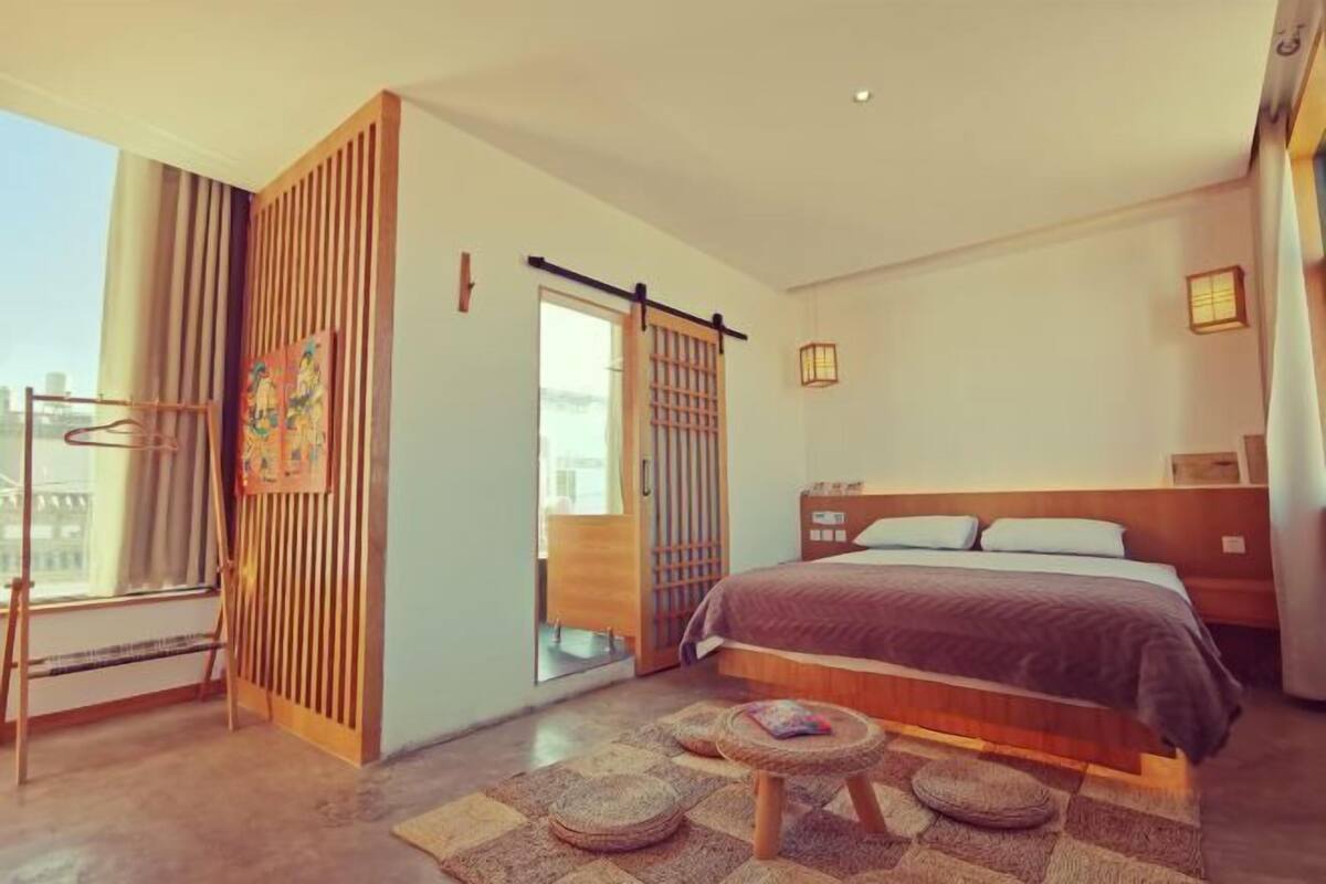 A modern hotel room with a large bed, a sliding door, a small seating area, and a view of the city.