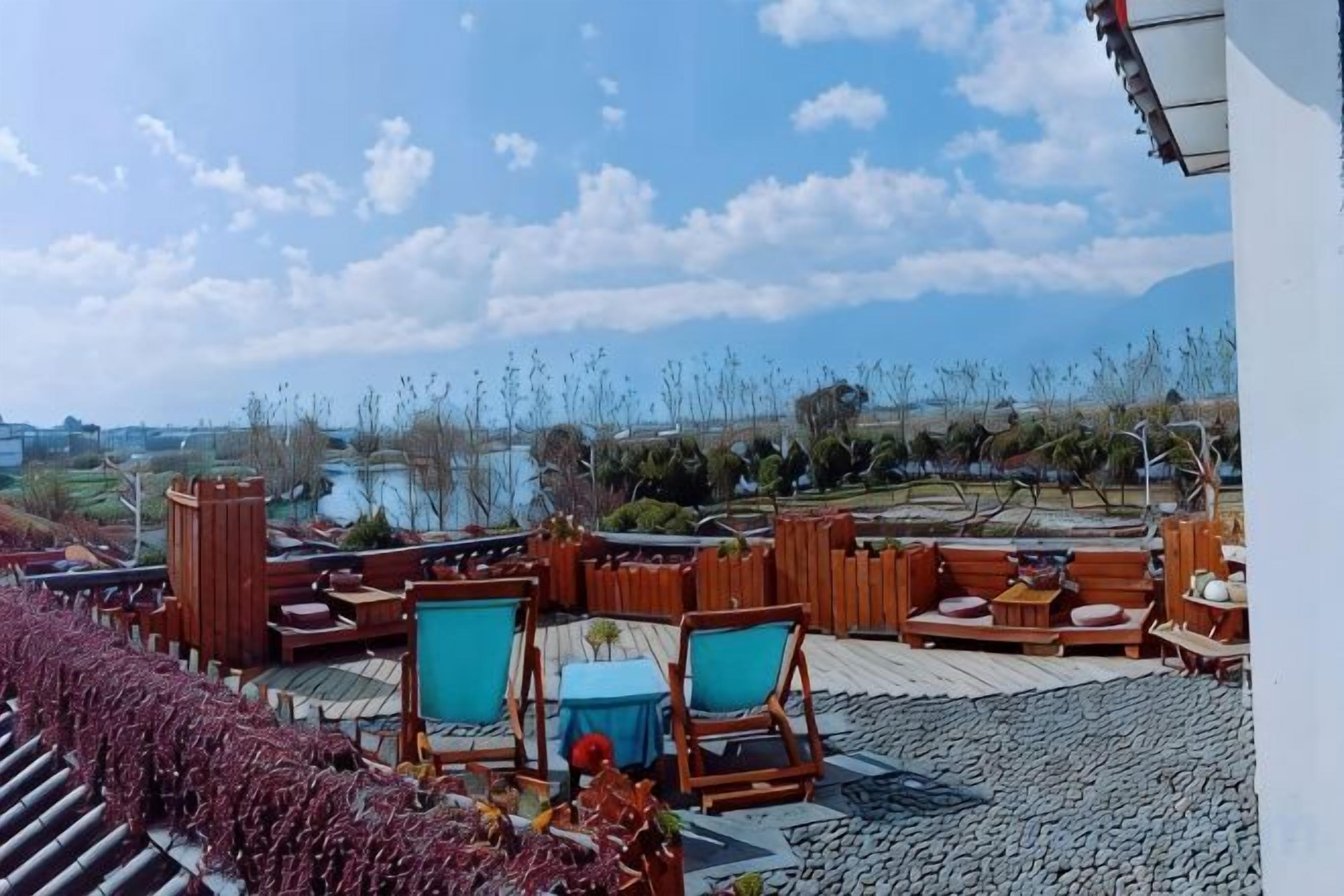 Un espacio al aire libre con mobiliario de madera y vistas a un lago y paisaje distante.