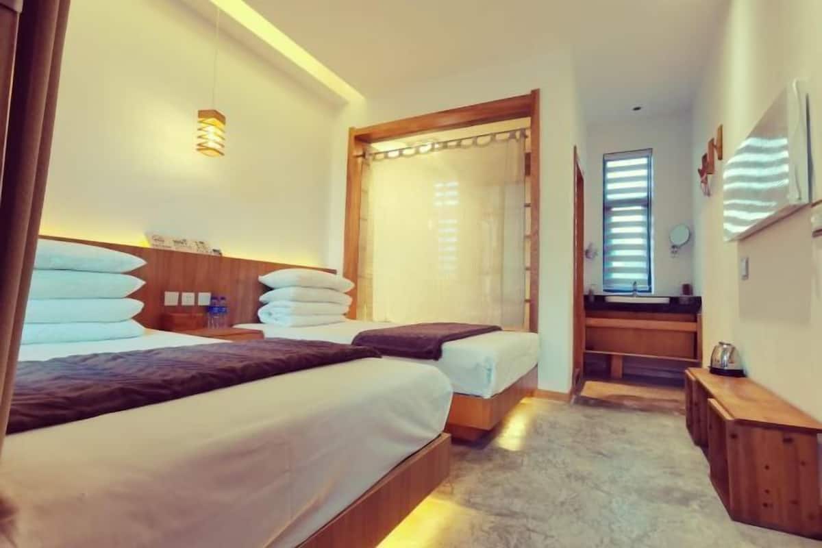 A hotel room with two beds, a wooden headboard, a small desk, a mirror, and a window with blinds.