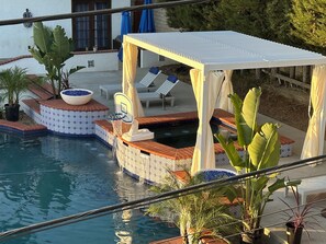 Zona de piscina con área de descanso cubierta, sillas de salón y una piscina pequeña.