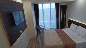 Ein Hotelzimmer mit Bett, Fernseher an der Wand, Fenster mit Vorhängen und Blick auf die Stadt.