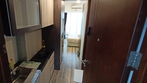 Ein schmales Entree mit Küchenbereich links, einem Bett mit Fenster in der Mitte und einer Tür rechts.
