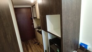 Ein schmaler Flur mit Holzboden, einer geschlossenen Tür und einer kleinen Küchenzeile mit Schränken und einer Mikrowelle.