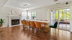 Un comedor amplio con una mesa larga, múltiples sillas, una chimenea y grandes ventanas que ofrecen vistas al exterior.
