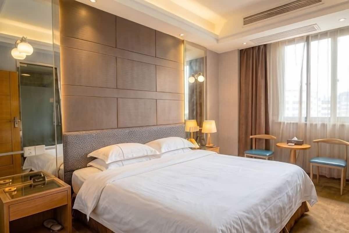 Habitación de hotel con una cama grande, una mesita de noche, un espejo, una pequeña mesa con lámpara y una silla.