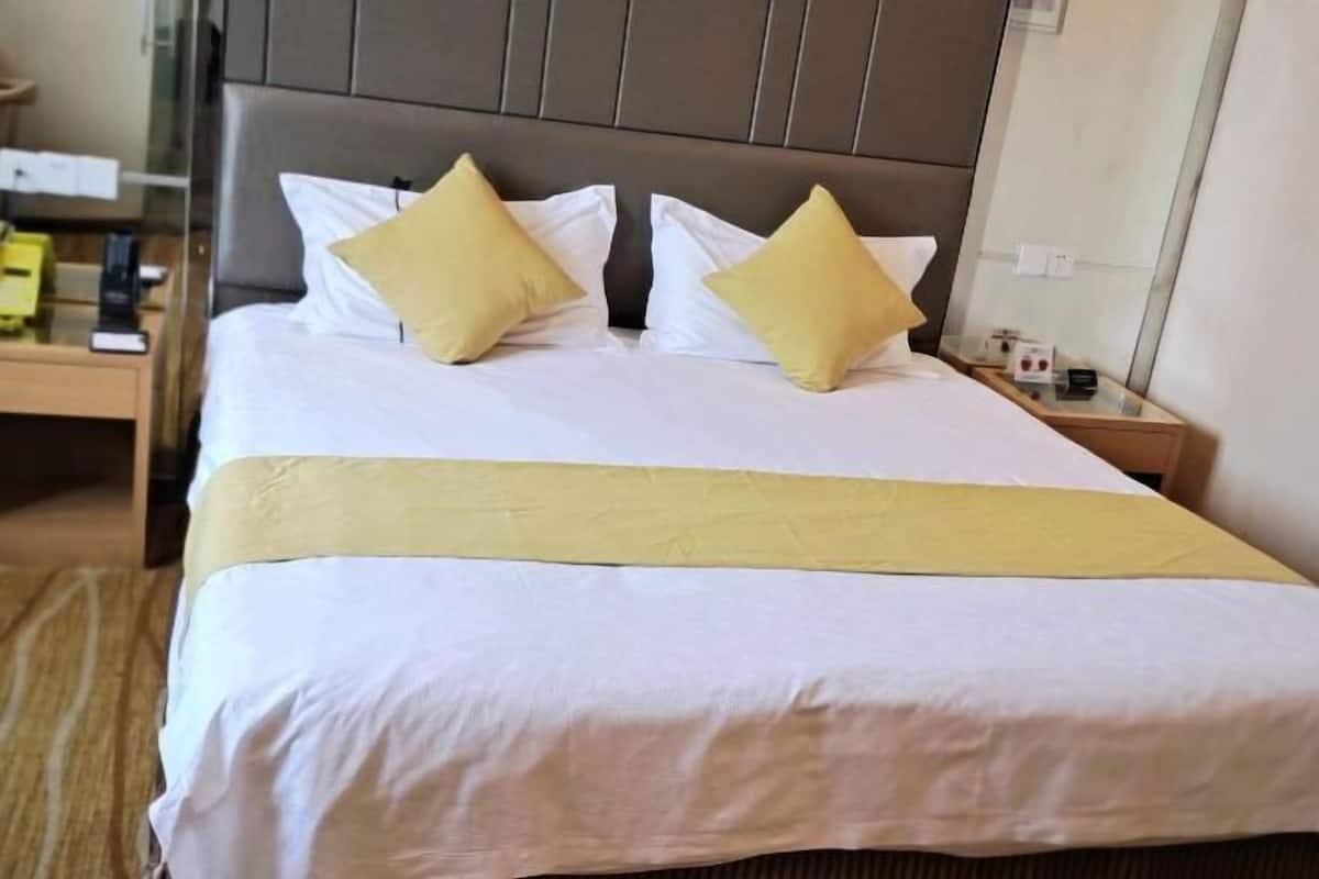 Una habitación de hotel con una cama, dos almohadas, una mesita de noche y un tocador.