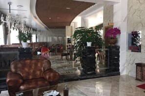 A lobby with a leather armchair, a reception desk, a large potted plant, and a chandelier.