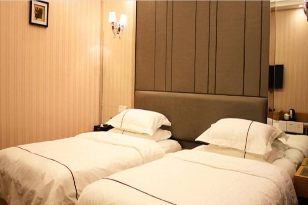 Habitación de hotel con dos camas, cabeceros, mesitas de noche, una lámpara de pared y un cuadro enmarcado.