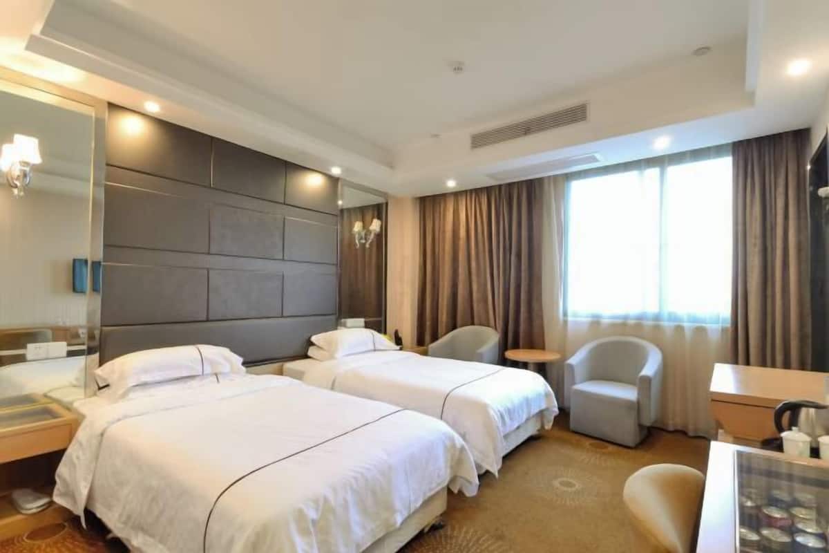 Habitación de hotel con dos camas, una zona de estar con una silla, un escritorio, un espejo grande y una ventana con cortinas.