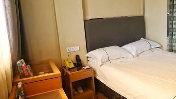Ein Hotelzimmer mit einem Bett, einem Nachttisch mit Telefon und Lampe, einem kleinen Holztisch und einem Schuhregal.