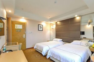 Habitación de hotel con dos camas, un escritorio, una silla y una mesita pequeña. Se ve una puerta con un cartel, un cuadro en la pared y una lámpara sobre la cama.
