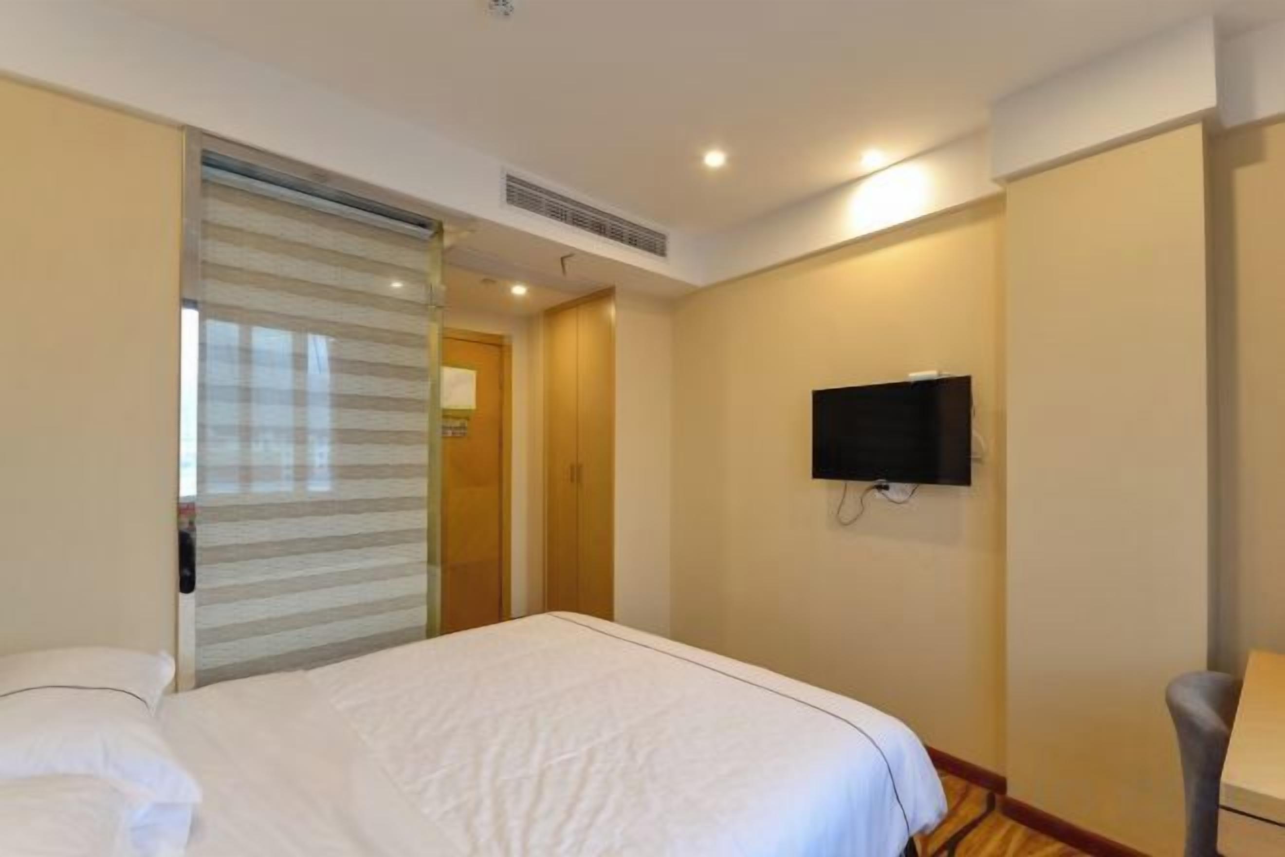 Una habitación de hotel con una cama, un televisor en la pared y una puerta que da a otra habitación.