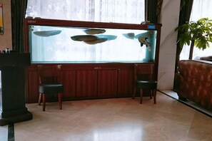 A room with a large fish tank, two chairs, a wooden cabinet, and a potted plant. - Xima Hotel (Taizhou West Station Branch) (Taizhou)
