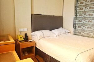 Una habitación de hotel con una cama, una mesita de noche de madera, un teléfono y un pequeño estante con pantuflas.