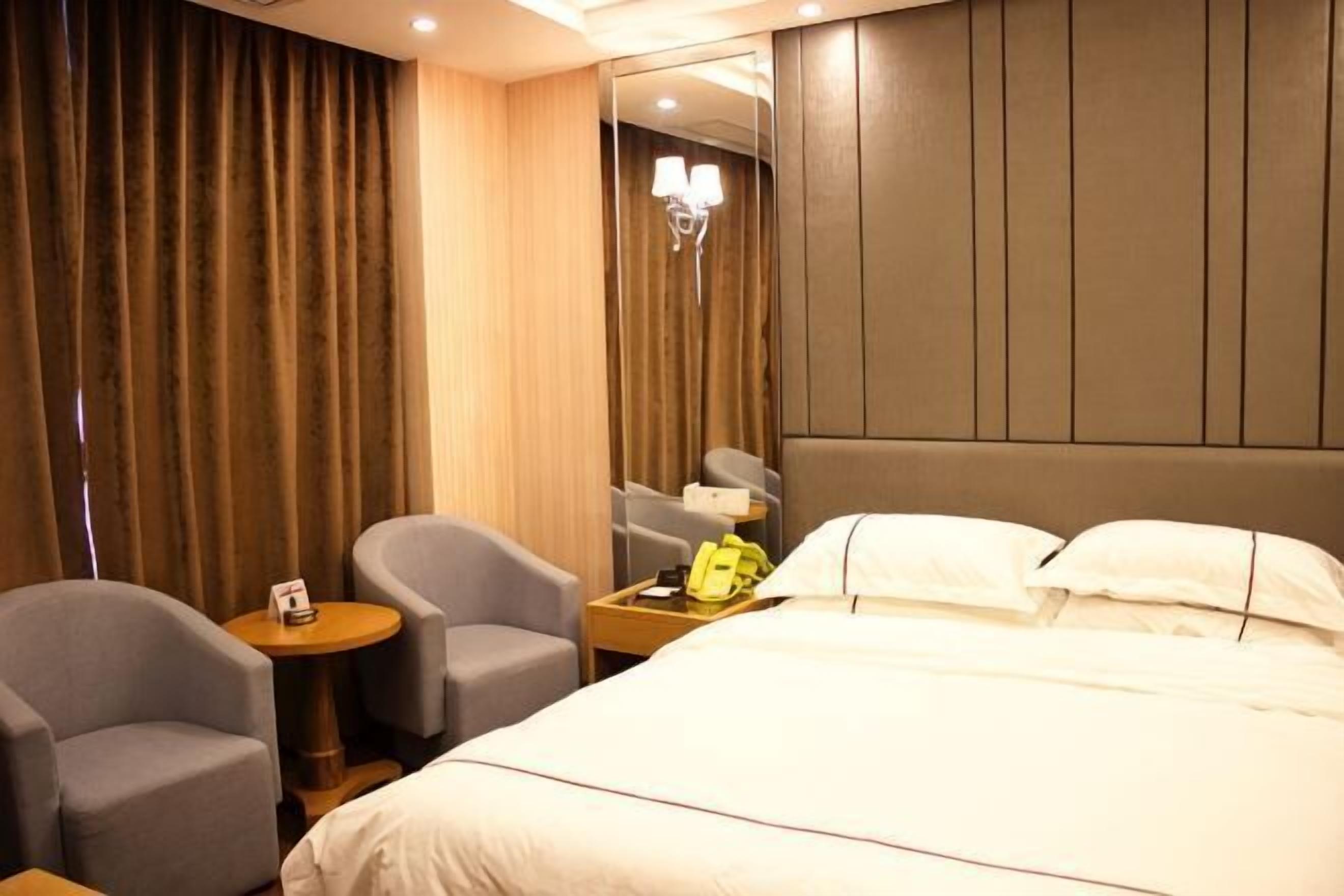 A hotel room with a bed, two armchairs, a small table with a lamp, and a mirror.