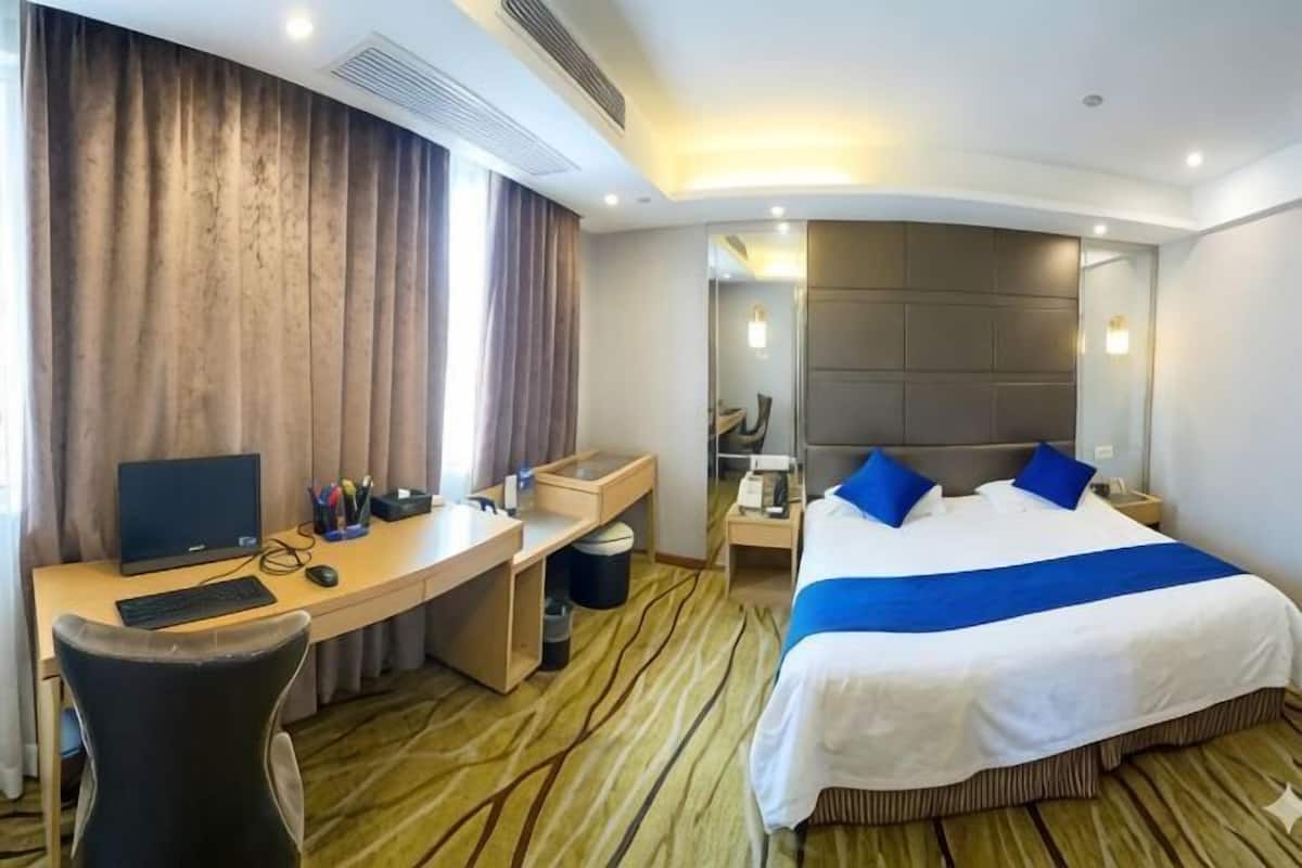 Una habitación de hotel con cama, escritorio, silla y un espejo grande.